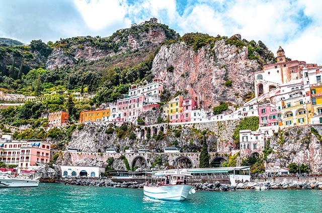 Pastel coloured house rise up the green mountain side from the turquouise waters of the Amalfi coast