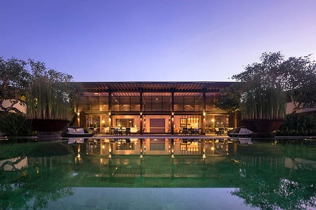 A luxurious wooden resort looking out to the inviting pool Infront lit up in early evening 