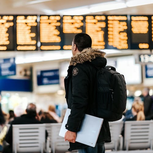 A man carrying a laptop and rucksack looks at announcement boards within an airport