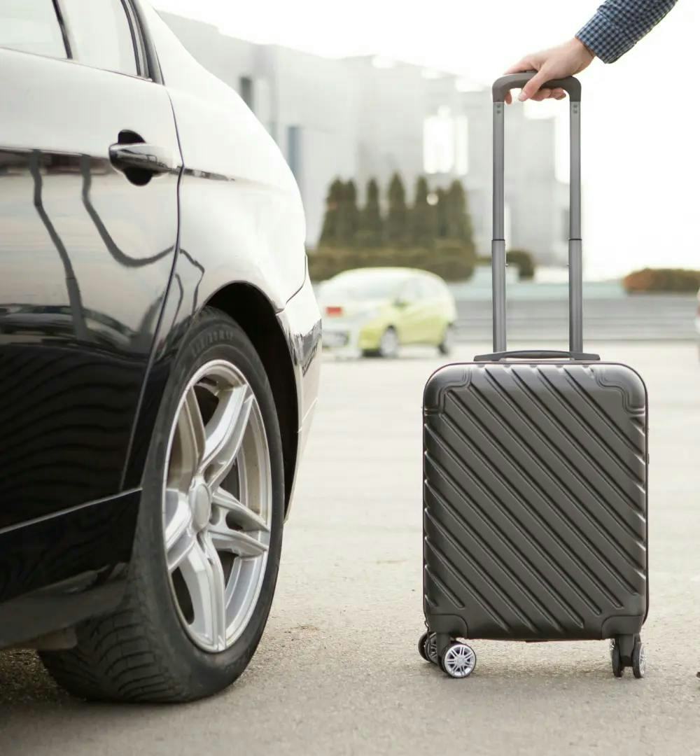 A man standing with a suitcase next to a private car at the airport