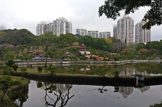 Traditional Chinese styled buildings next to a lake with large apartment buildings in the background 