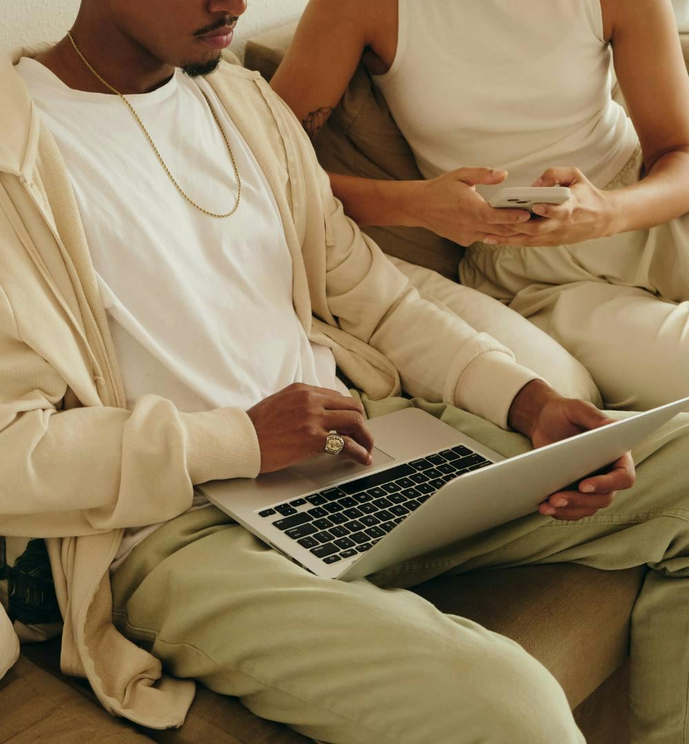 A couple sat down using a laptop and a mobile phone