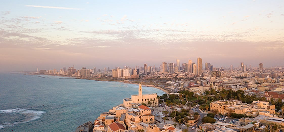 Tel Aviv skyline in the early evening with the sun casting a warm glow over the city. The traditional city sites by the sea with the modern and futuristic skyscrapers looming in the distance 