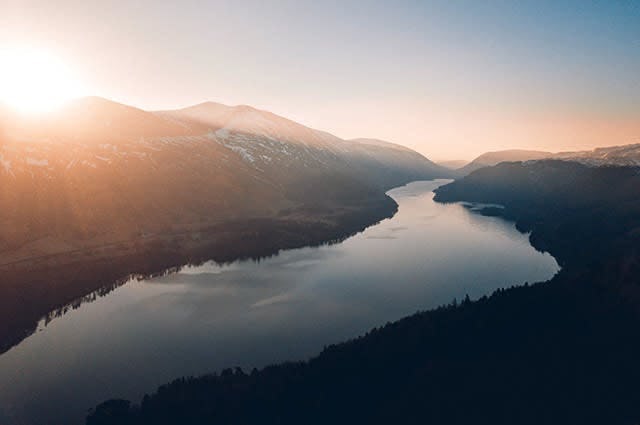 A sunset shot looking down at the lake district showing a long lake, mountains. 
