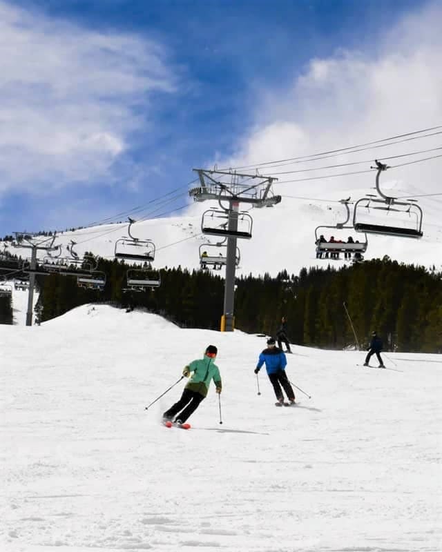 A shot of people skiing down a slope with a ski lift behind them
