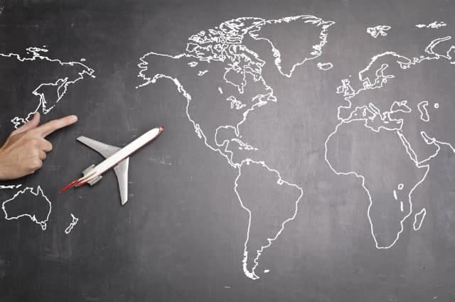 Chalkboard with drawing of the world map and a plane model with a hand pointing 