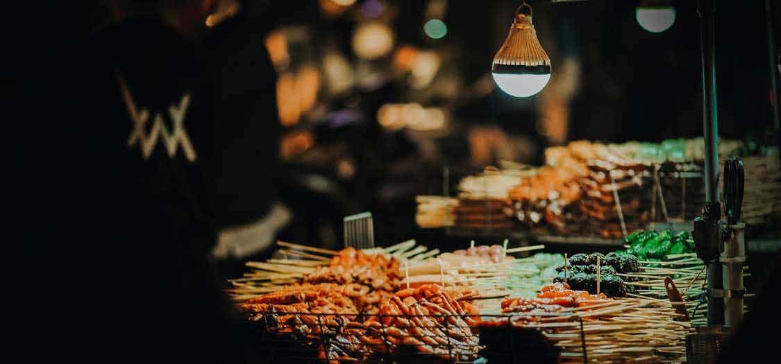A photo of a street food stall taken at night, with lamplight highlighting skewered foods