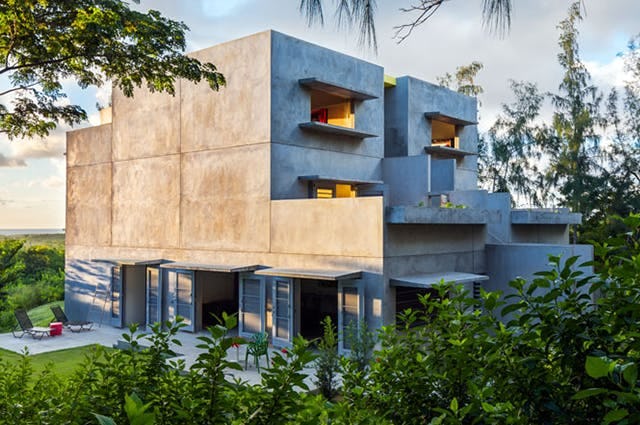 A grey concrete Brutalist style of architecture building nestled in the lush green foliage 