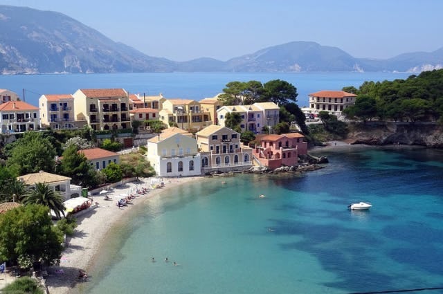 Kefalonia. Blue sea, lined with houses. Small beach, mountainous background.