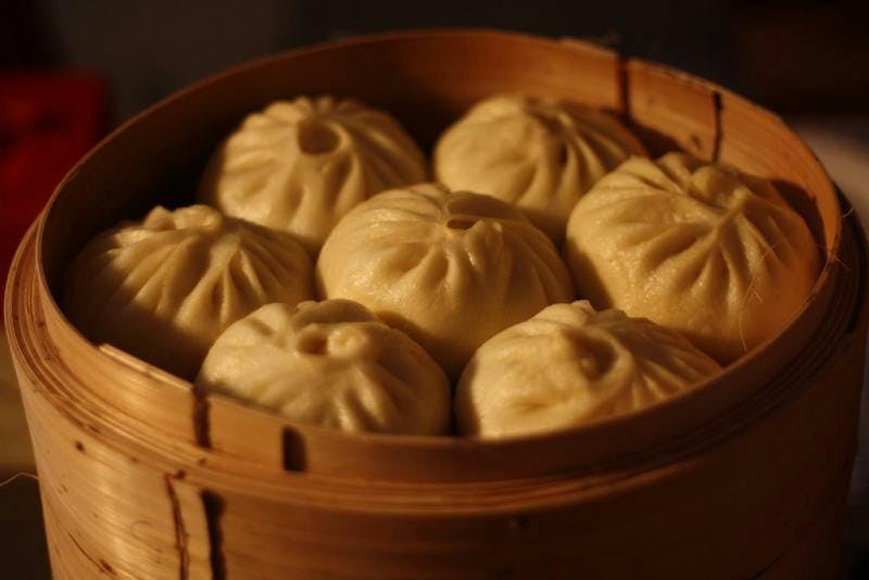 A close up shot of 6 baozi in a wooden dish