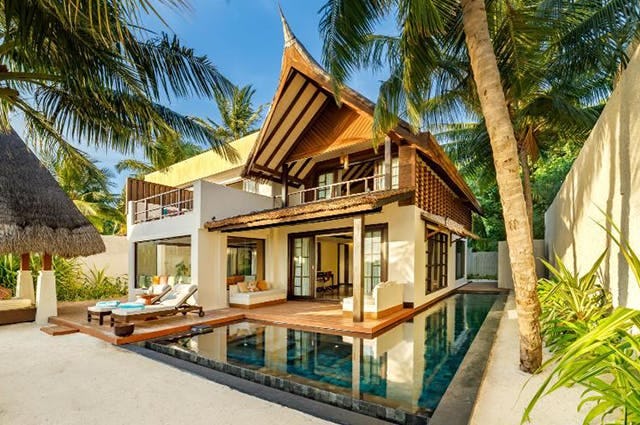 A luxury Mauritian beach house with wrap around swimming pool and palm trees casting shade over the courtyard  