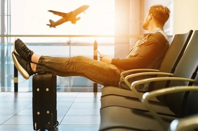 man chilling in an airport departure seating area while watching a plane depart through the window