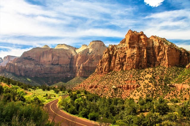 A shot following a road heading towards the Grand Canyon National Park, depicting the high ragged rocks and green shrub along the roadside. 