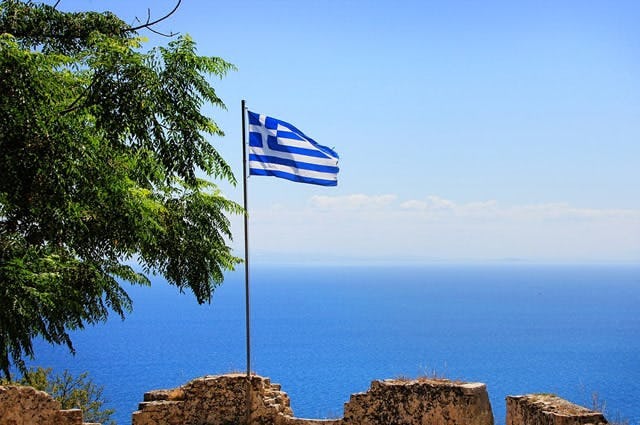 A greek flag fluttering on a cliff by the sea in Mani 
