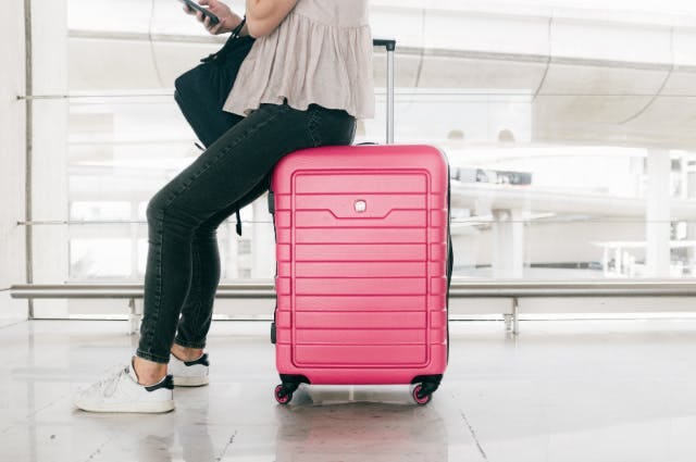 Picture of woman sitting on a pink suitcase at the airport