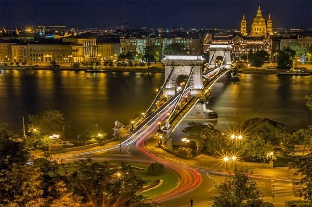 A view of the Széchenyi Chain Bridge crossing the Danube river at night in Budapest with the street lamps lighting the city