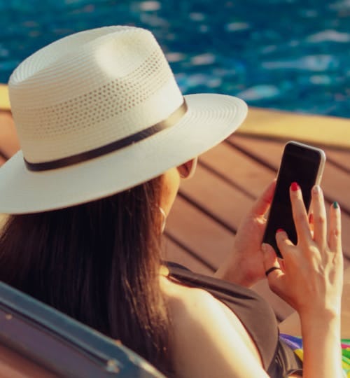 A woman looking at her phone sitting by a swimming pool