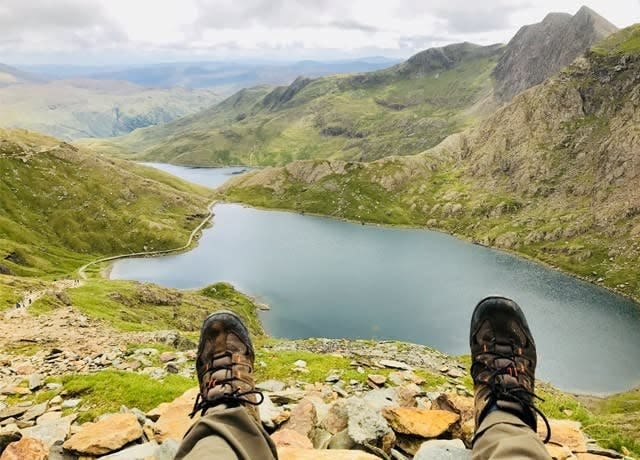 A shot taken from the walk up Mt Snowdon in Wales. The feet of a walking in the foreground with a lake below