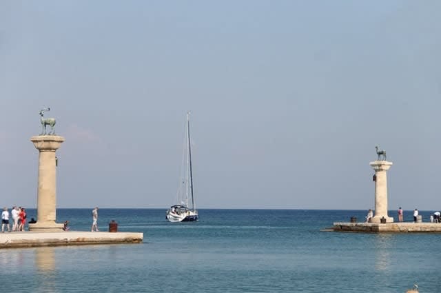 A boat sailing into Mandraki harbour in between two stone podium 