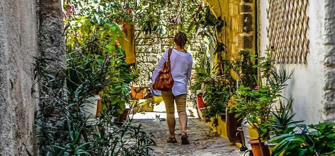 Woman wearing sandals walking through a small street somewhere hot, with warm light and potted plants
