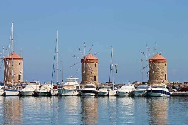 Three windmills set behind a row of yachts in a marina 