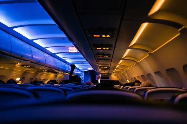 A photo taken of a dark cabin on a plane with blue aisle LED lights and the top of passengers heads