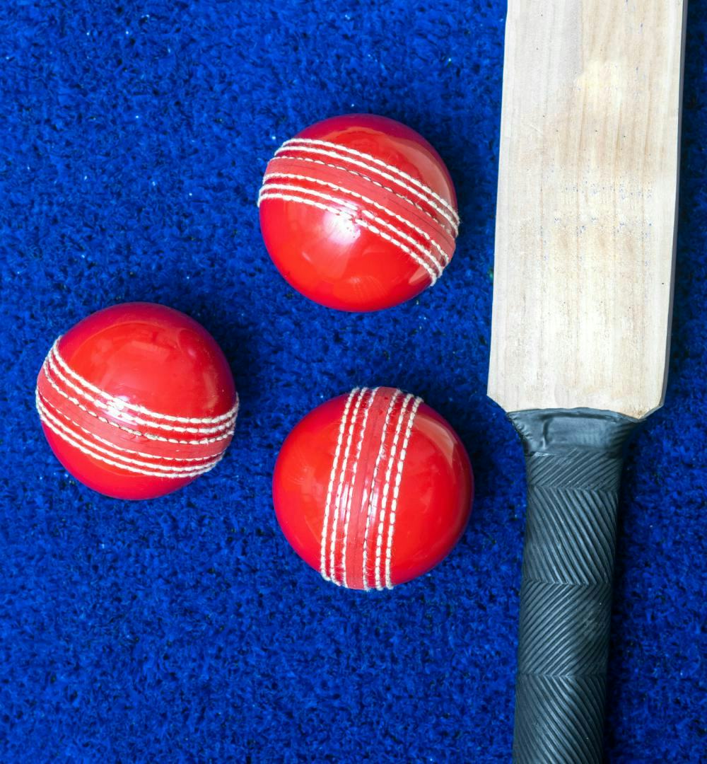 3 cricket balls next to a cricket bat