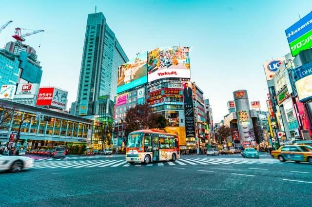 A colourful city shot of Tokyo, Japan, at a crossroads showing building advertisements, taxis and a bus