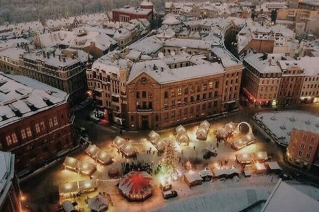 A shot looking down at a Christmas market in Riga, with the grand buildings covered in snow and the twinkling lights of the market