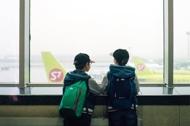 Two children looking at planes on a runway out of a window at the airport