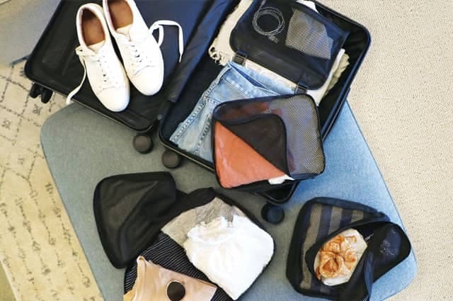 a shot looking down at an open suitcase and carry-on bag with items packed including jeans, trainers and a laptop bag and charger