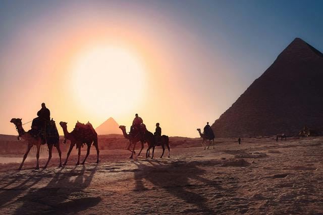 camel riders riding in egypt's desert through pyramids