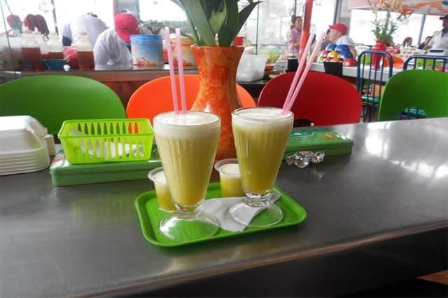 Two fresh fruit smoothies with pink straws on a green tray, taken in a cafe in Bogata