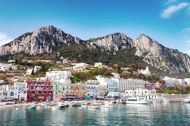 A view of Capri island from the sea with white villas and rocky coast
