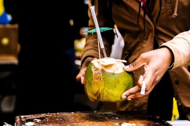 Someone lifting a fresh coconut which has been split open to have as a drink, with a straw and umbrella in it
