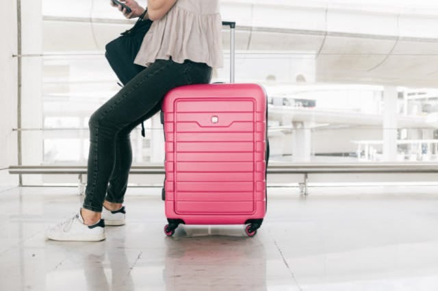Woman sitting on a pink suitcase