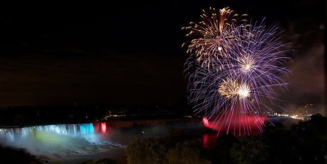 fireworks exploding over Niagra falls which is lit up in blue, white and red
