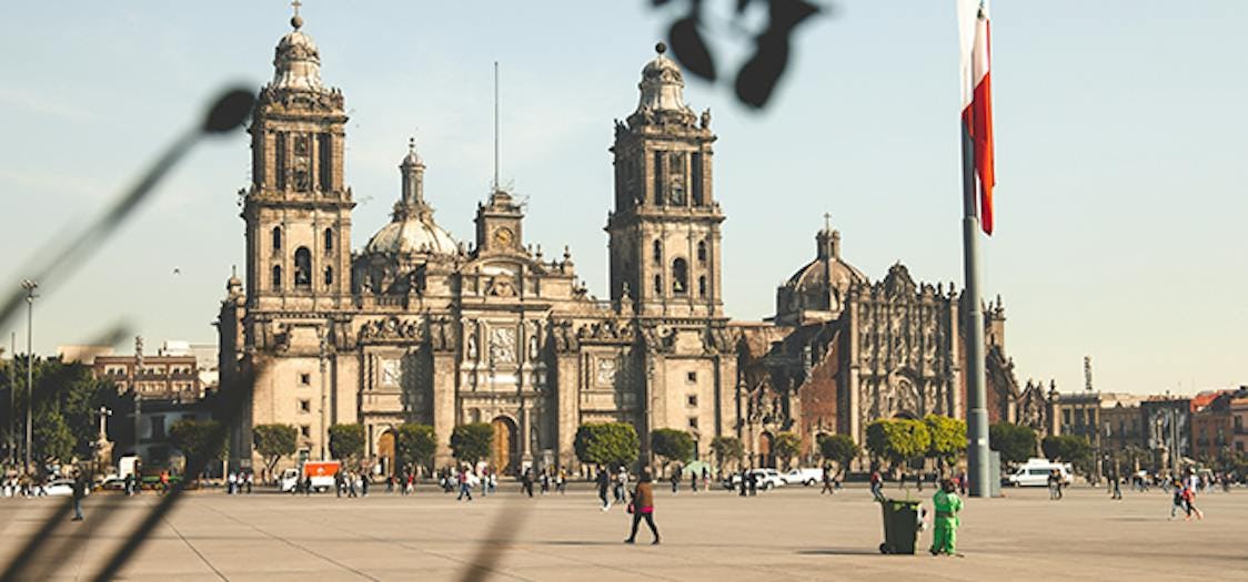 A stone cathedral in Mexico City with the Mexican flag to the right