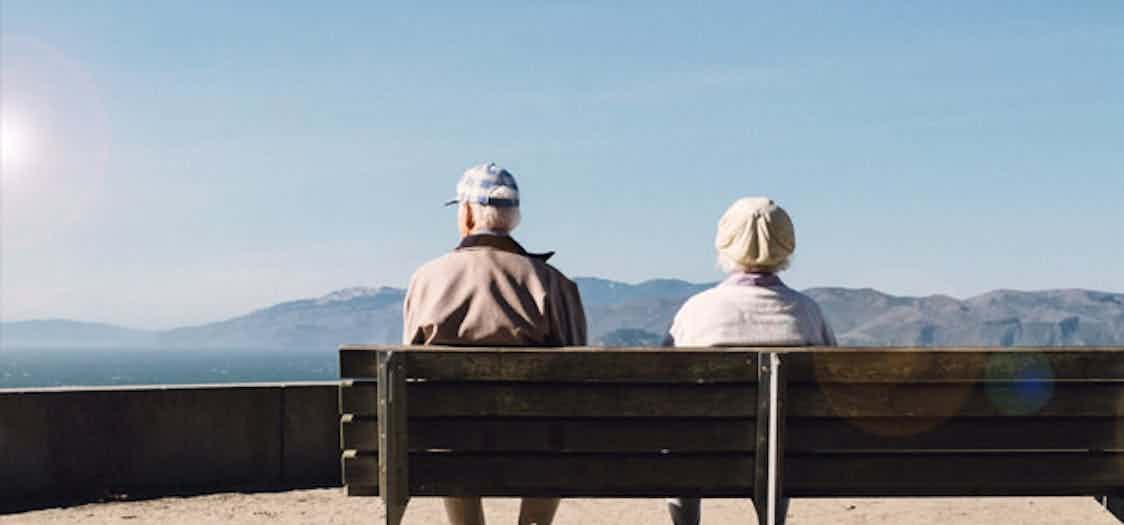 2 senior citizens sat on a bench looking out to sea