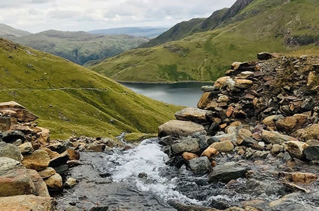 A shot taken from the walk up Mt Snowdon in Wales, with green slopes, rocks and a small lake