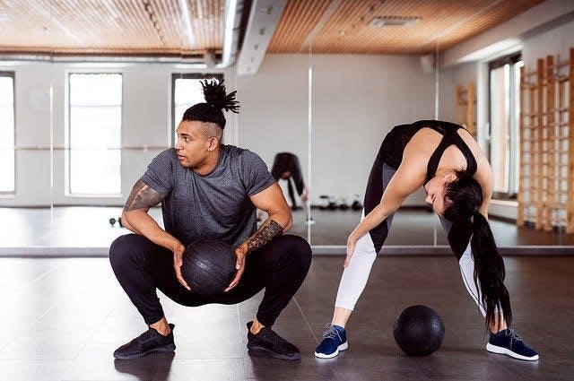 A shot taken inside a gym showing a man and woman both stretching in gym-wear 