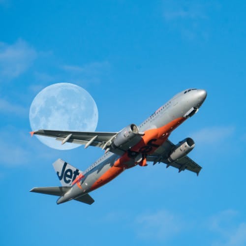 JetStar flying in clear skies with moon behind it 