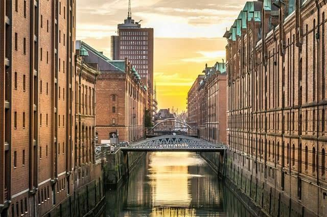 A photo taken in Hamburg, Germany. Shows industrial style red brick buildings and a low bridge over the waterway  