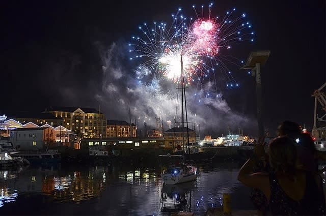 Fireworks celebrating the New Year in Cape Town harbour lighting the city and moored boats. 