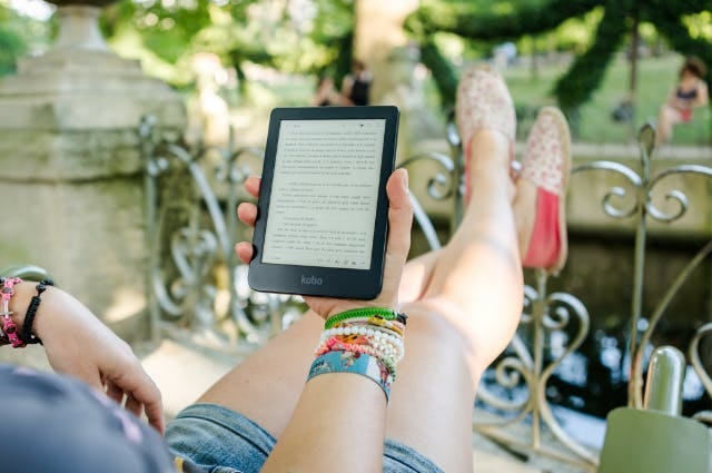 woman relaxing in a garden on a sunny day while reading from an e-reader
