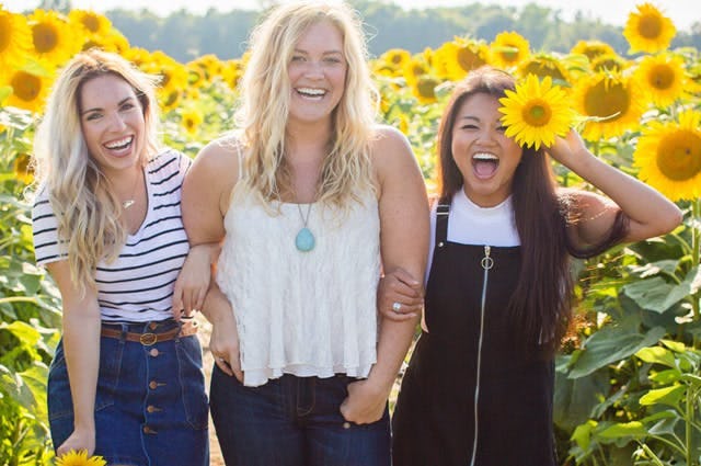 3 people standing and smiling in a field of sunflowers