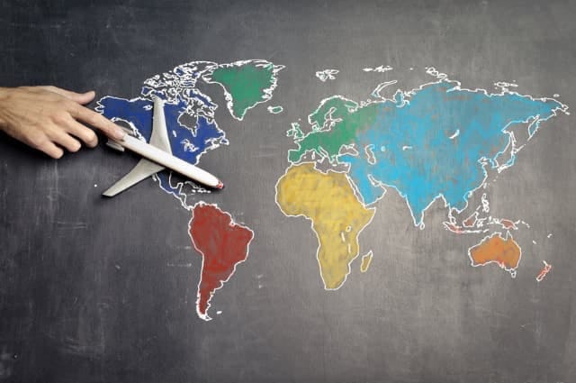multicoloured map of the world with a plane being pushed across it by a hand