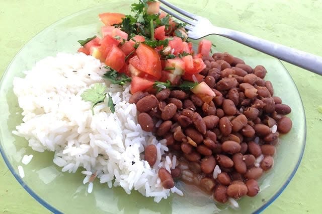 A plate of Brazilian rice, beans, tomatoes and coriander with a metal fork sitting on the plate