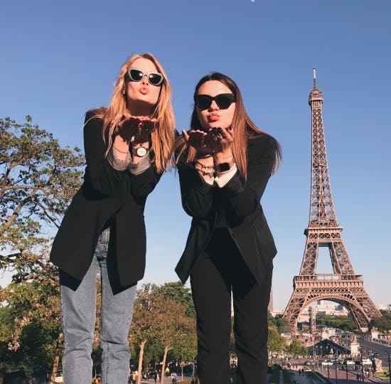 Two women blowing kisses in front of the Eiffel Tower