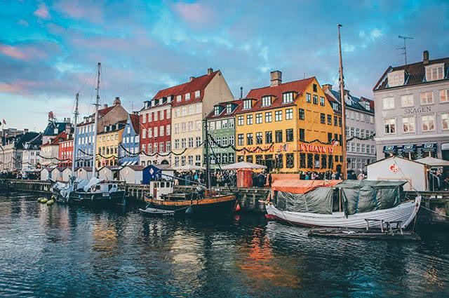 A promenade in Copenhagen with boats moored and colourful houses lining the shore 